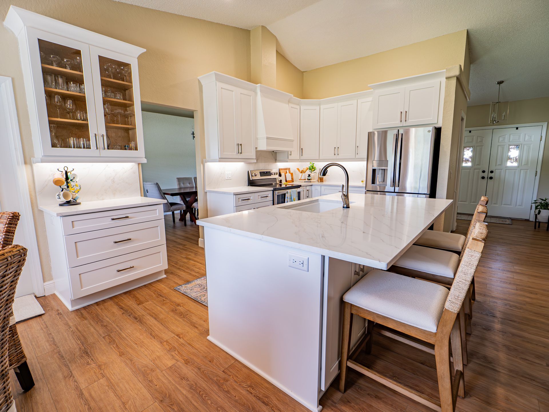 Modern white kitchen with island seating, stainless steel appliances, and wooden floors.