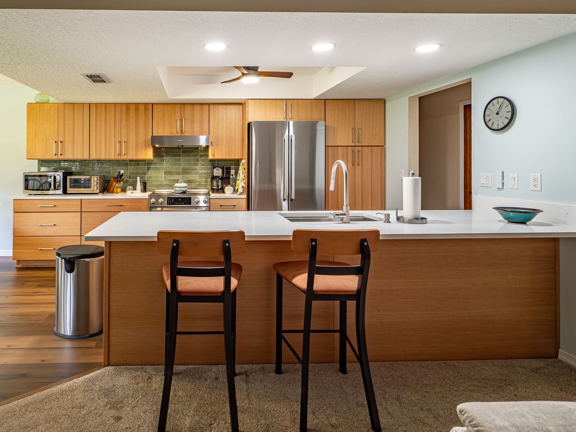 Modern kitchen with wooden cabinets, island, stainless steel appliances, and two bar stools.