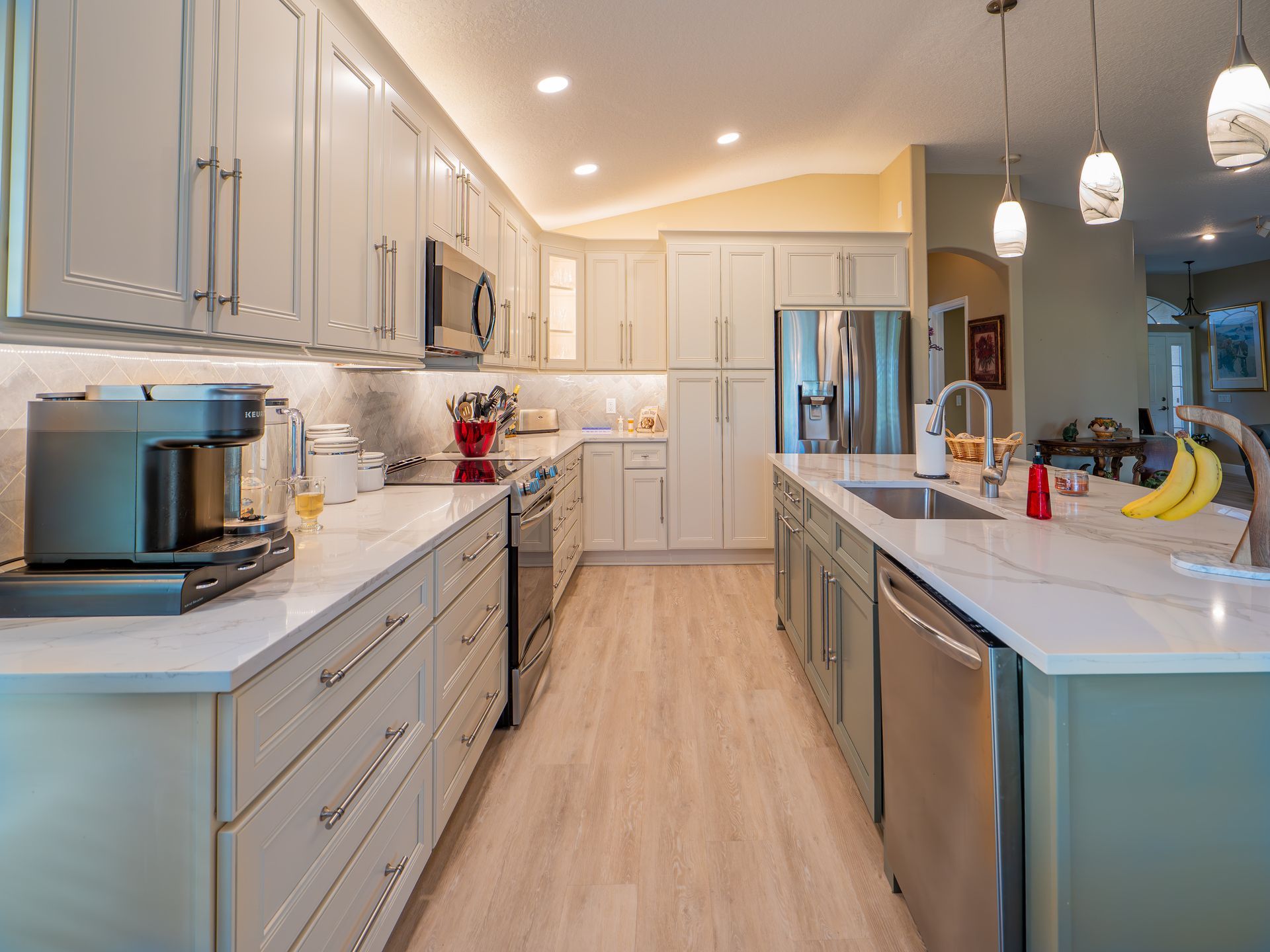 Modern kitchen with light green cabinets, marble countertops, stainless steel appliances, and wood flooring.