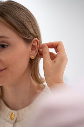 Person adjusting a small gold earring, close-up against a soft white background