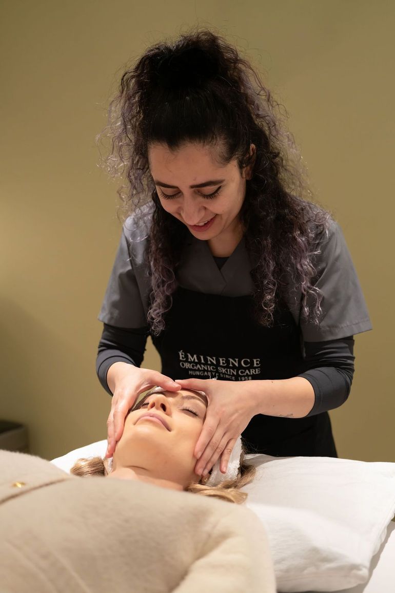 Massage therapist giving a facial treatment to a client on a spa bed