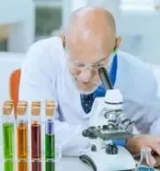 Scientist examining a sample through a microscope beside colorful test tubes in a lab