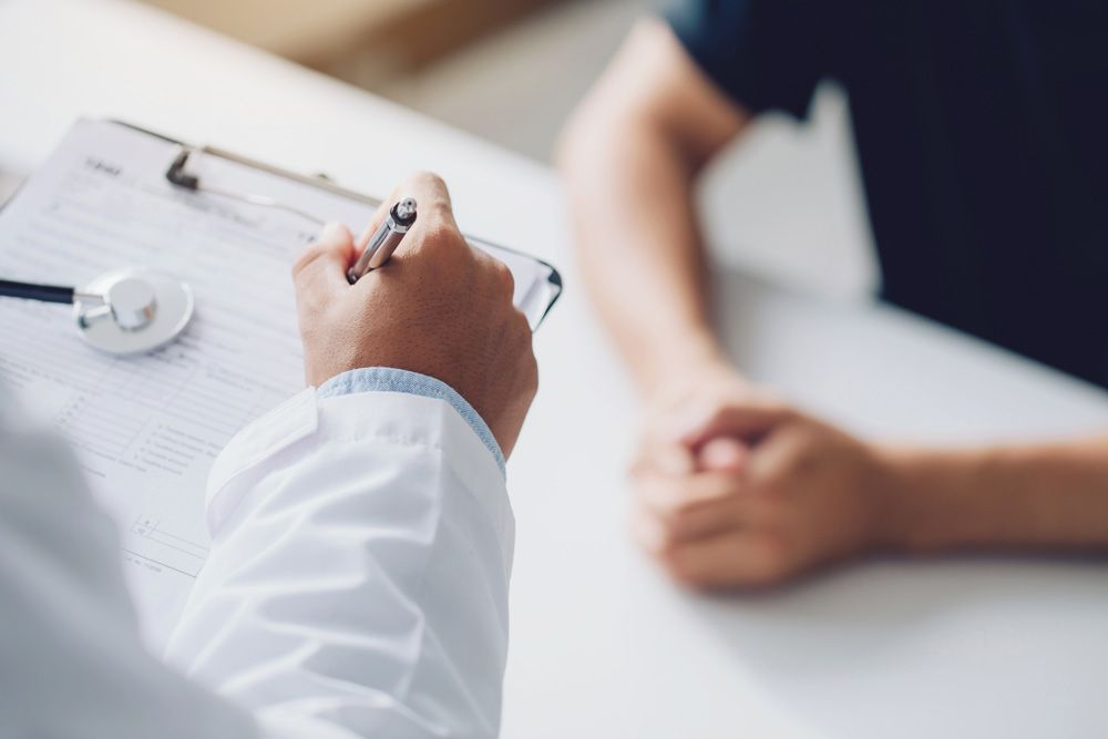 Doctor writing notes during a patient consultation at a desk