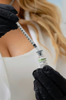 Gloved hands drawing liquid into a syringe from a vial, with a blurred person in the background