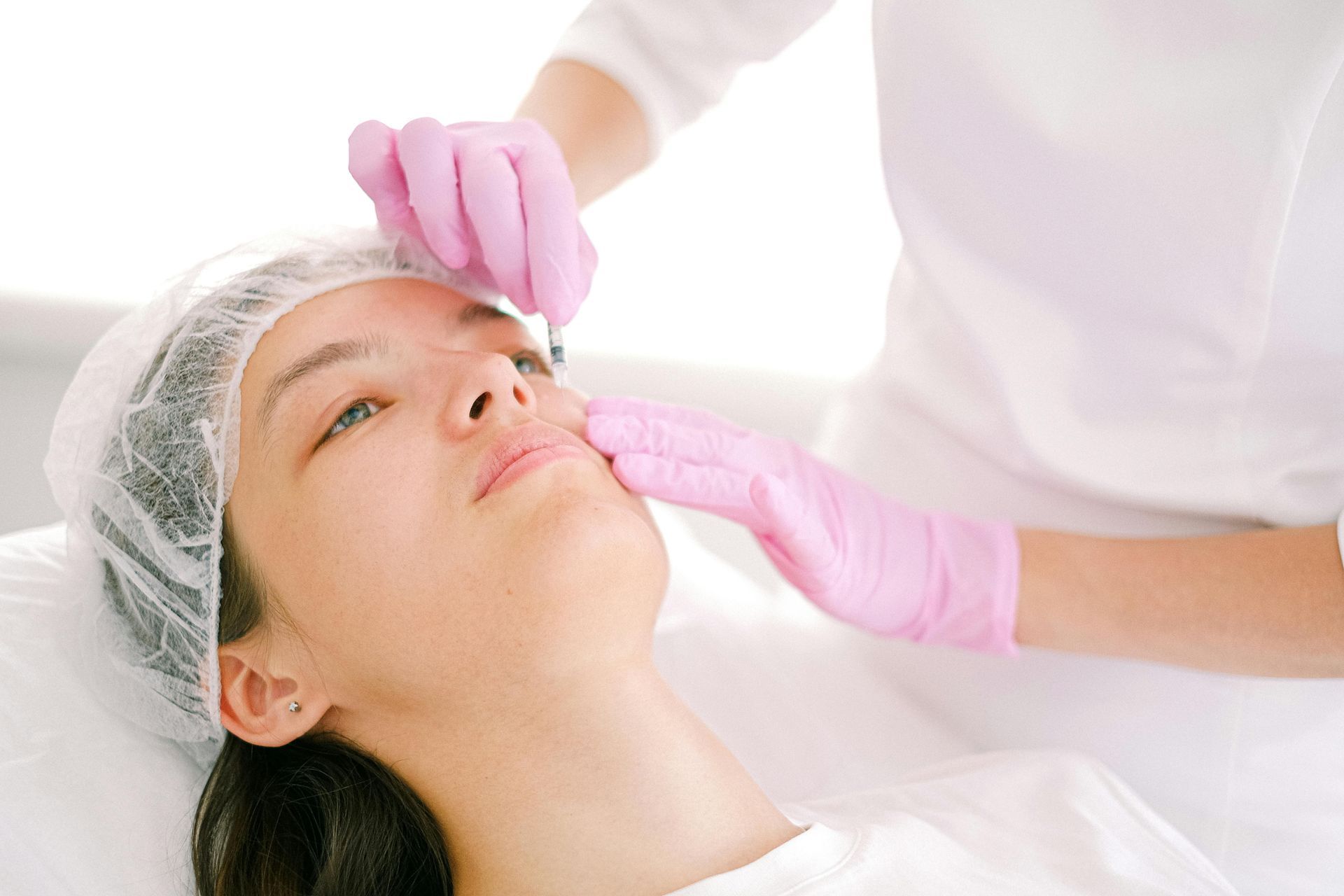 Aesthetic facial treatment with gloved hands applying product to a reclining client
