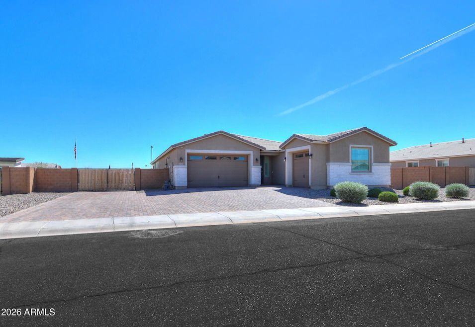 A single-story tan house with a paved driveway and a two-car garage under a clear blue sky.