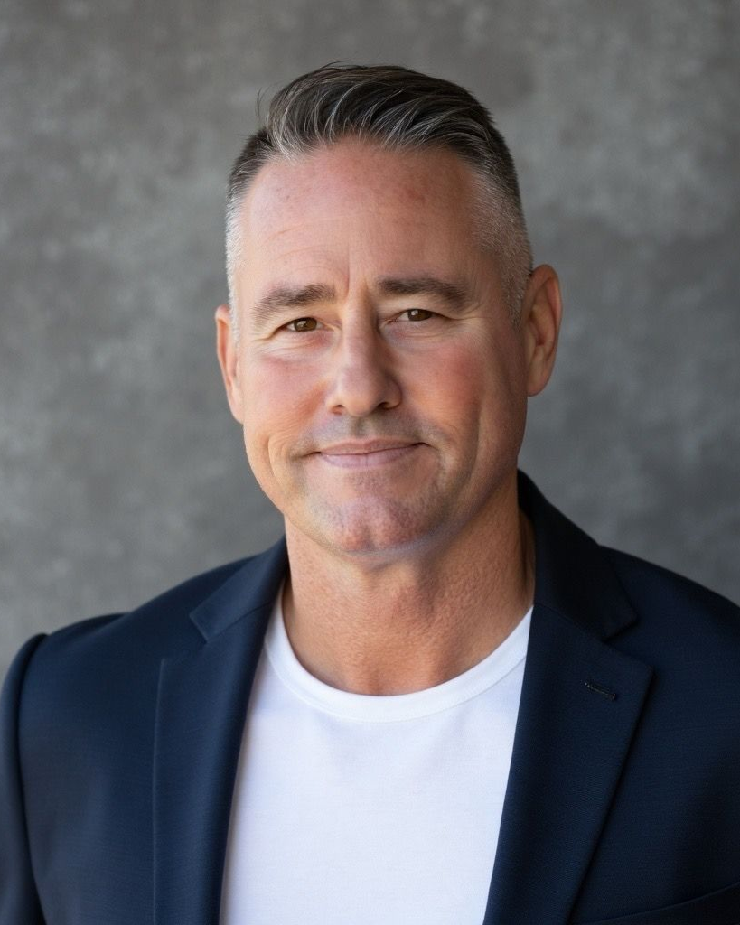 A brown and white hamster sitting upright in a wood-shaved cage with its front paws held together.