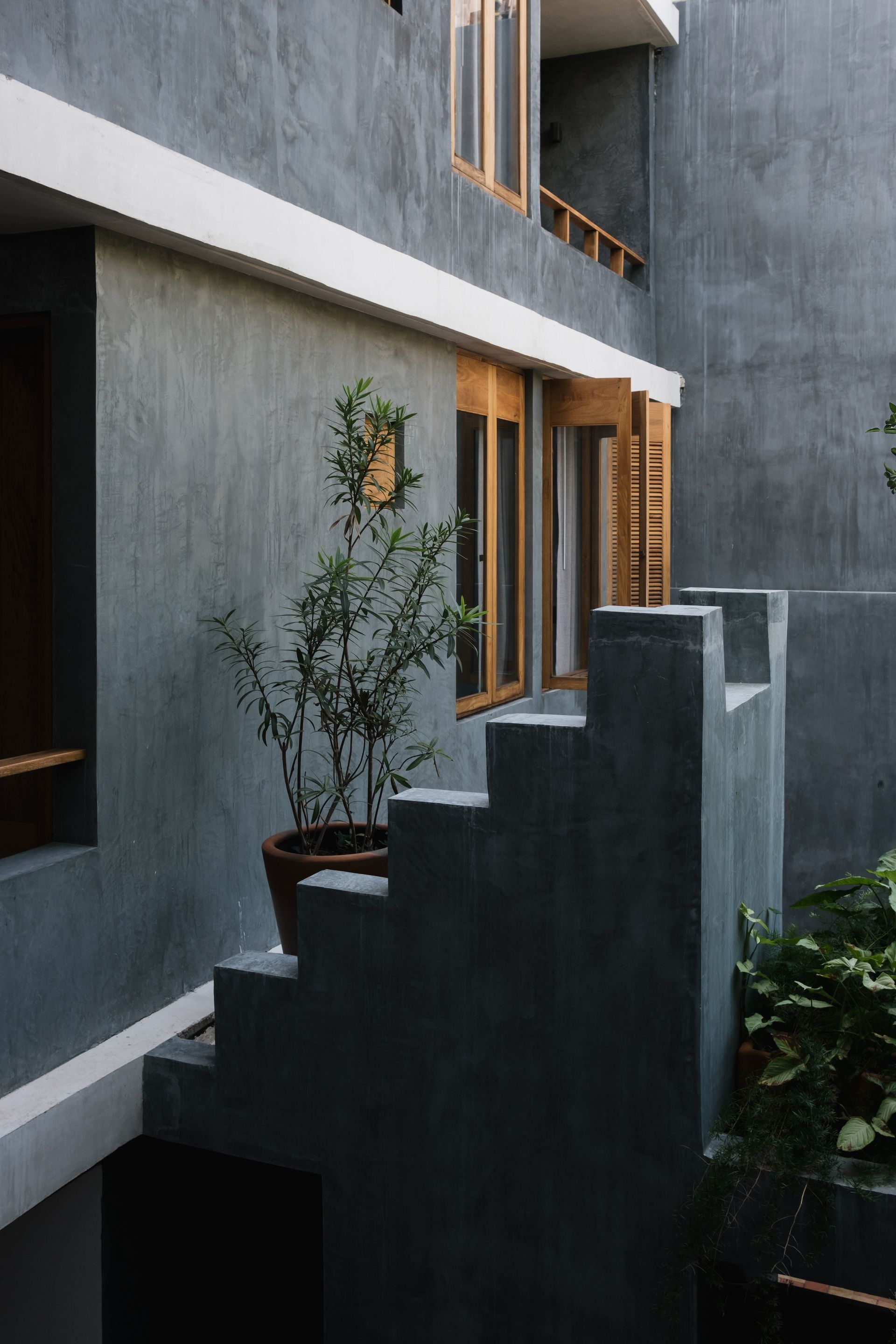 Exterior view of a building with gray walls, wooden windows, and a potted plant on steps.