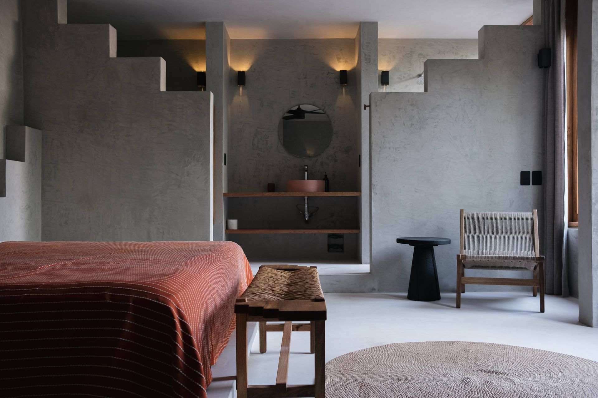 Bedroom with concrete walls, steps, and built-in vanity. Includes a bed, wooden bench, chair, and rug.