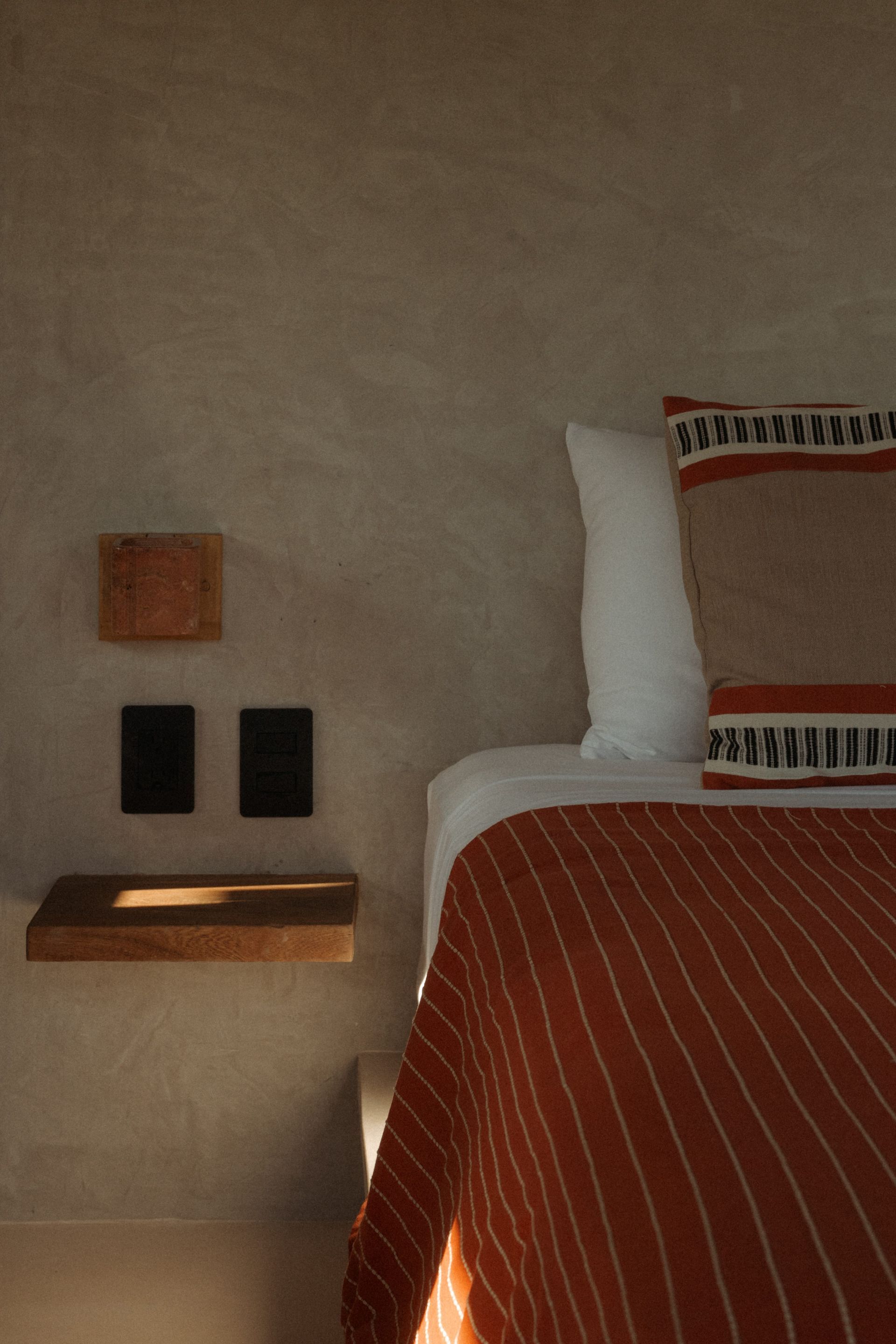 Bedroom corner with a bed covered in a striped orange blanket. 