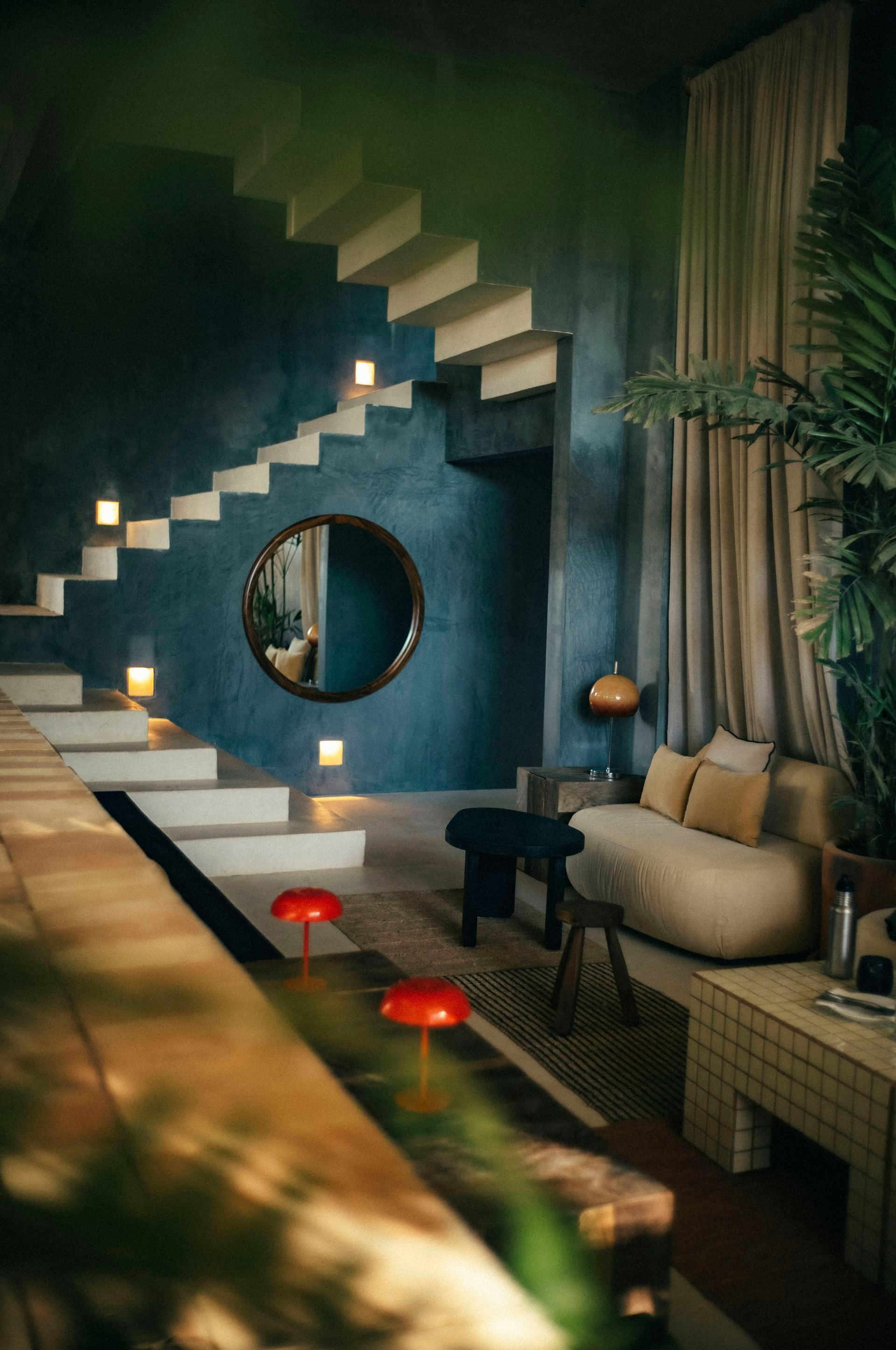 Interior with a blue textured wall, staircase, round mirror, and a beige sofa.