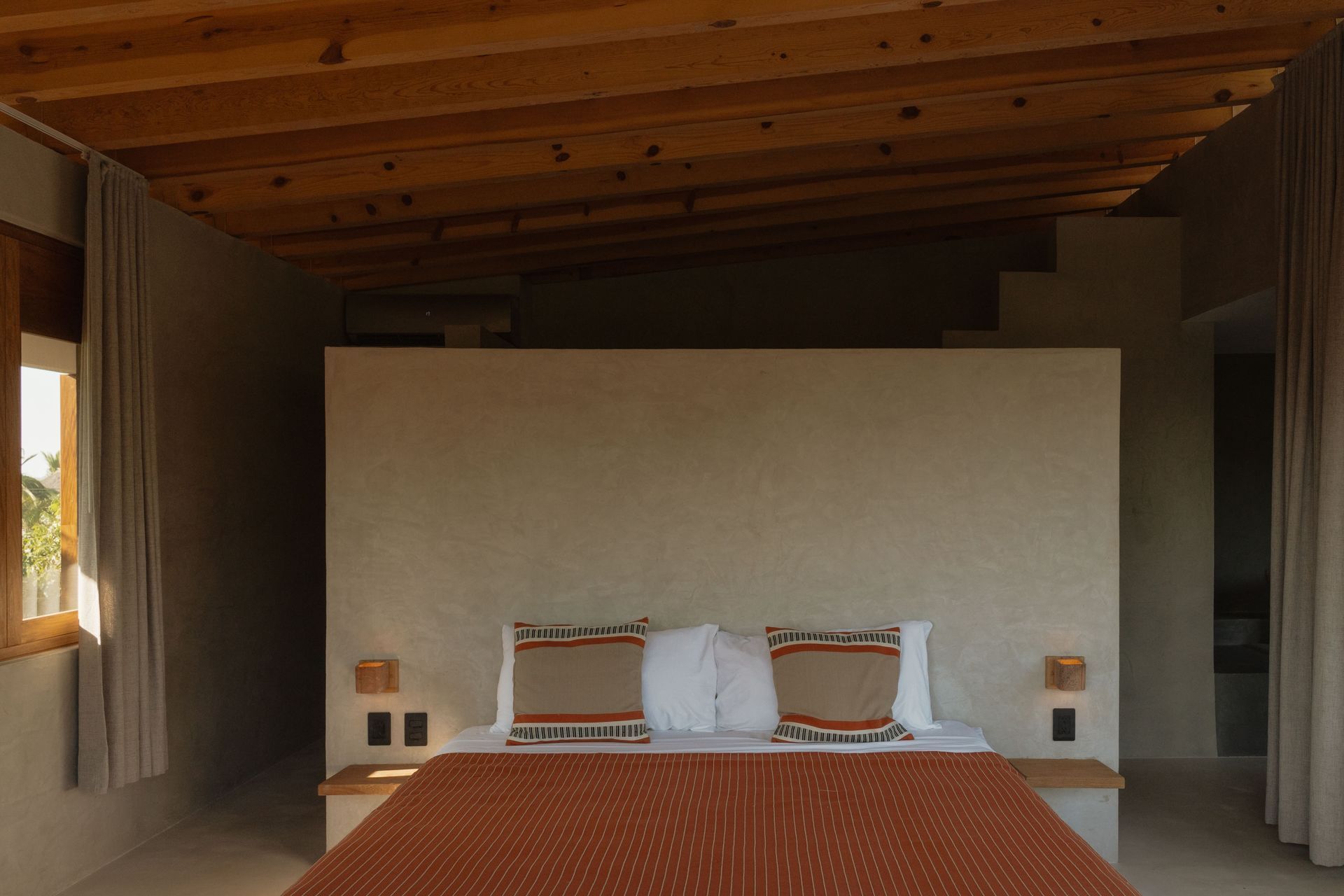 Bedroom with wooden ceiling, neutral walls, and bed with patterned textiles.