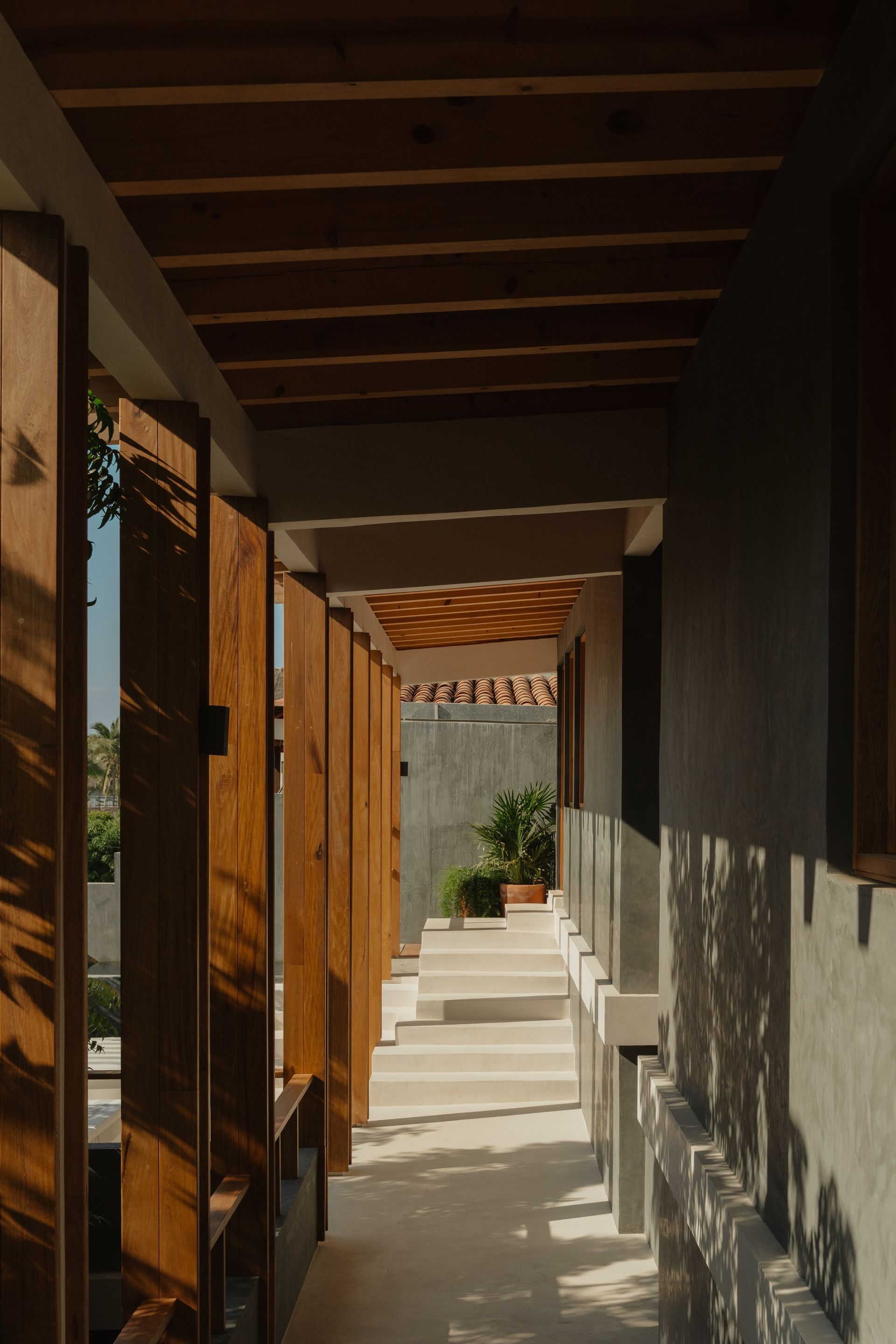 A covered outdoor walkway with wooden beams and vertical supports casting long shadows. 