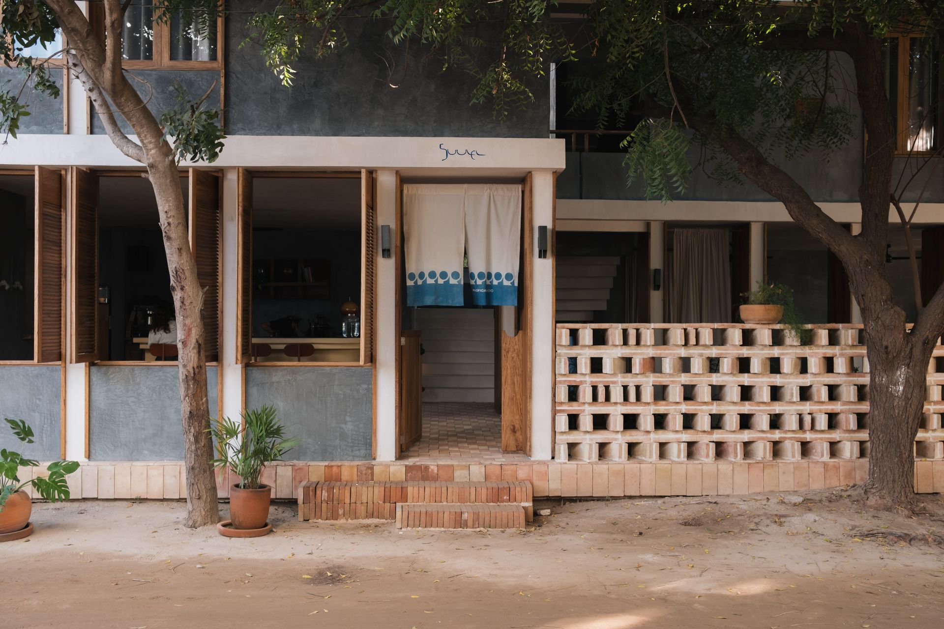 Exterior of a building with a blue and white fabric doorway, brick steps, and a partially open brick wall.