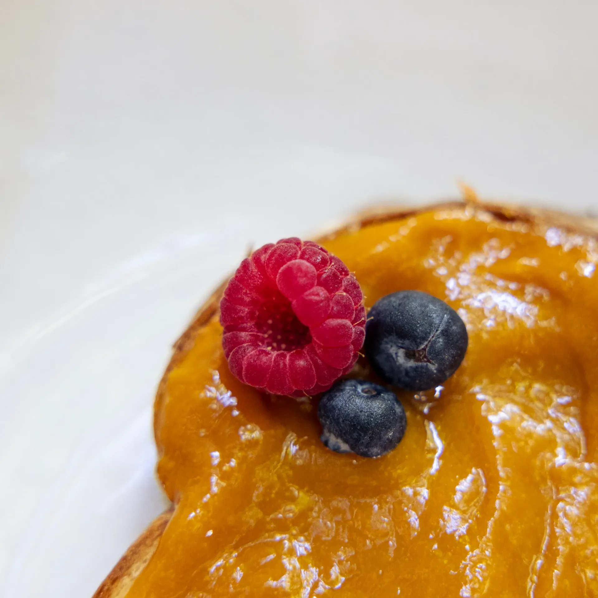 Toast with orange glaze, garnished with a raspberry and two blueberries.