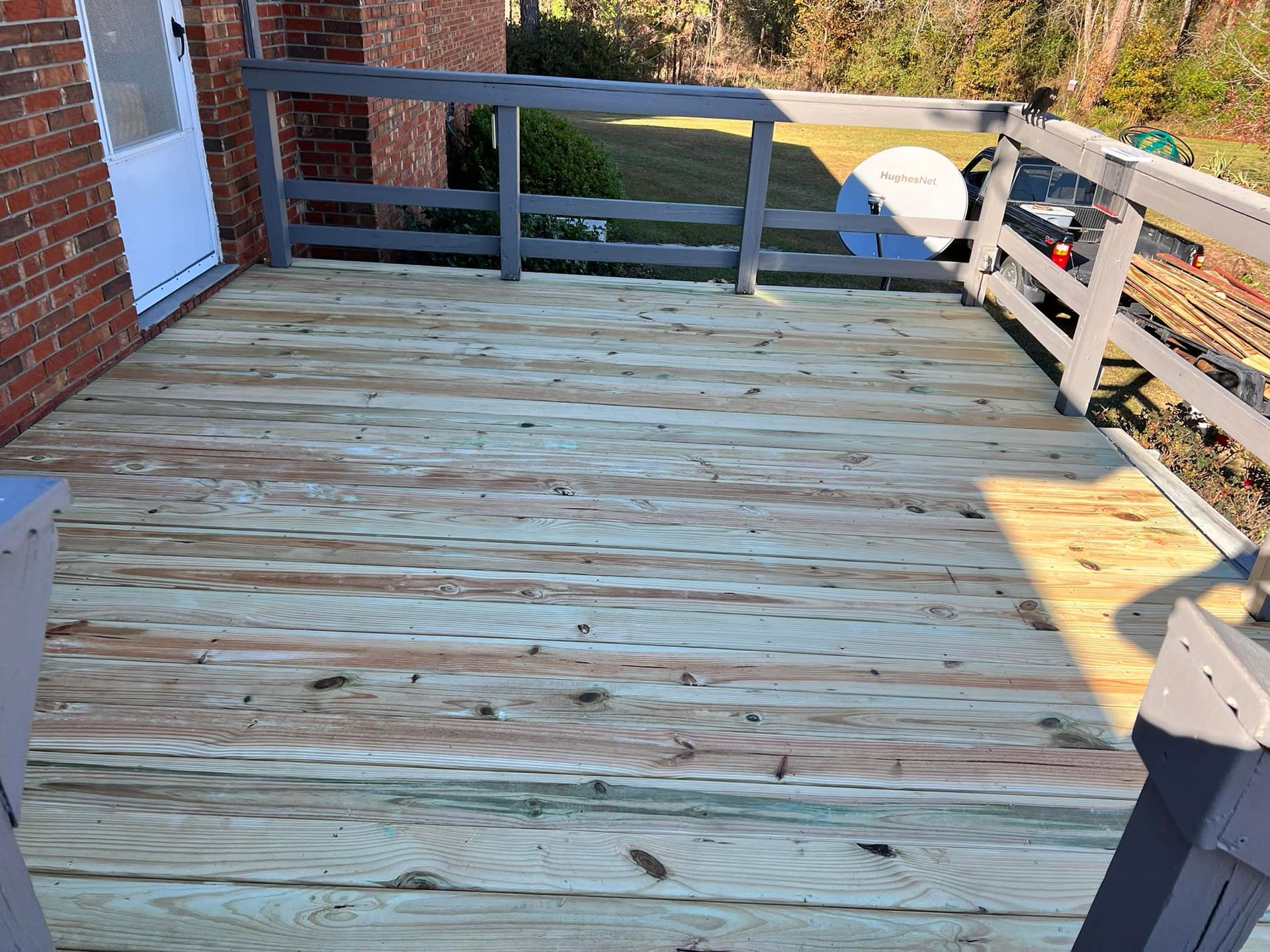 A wooden deck with a railing and a brick building in the background.
