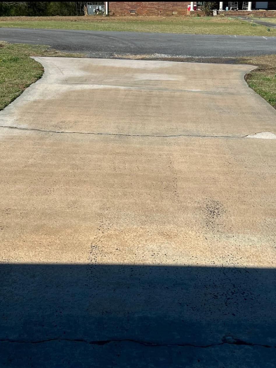 A concrete driveway leading to a grassy field with a house in the background.
