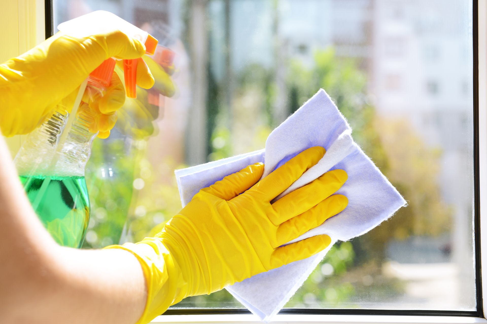 A person wearing yellow gloves is cleaning a window with a cloth.