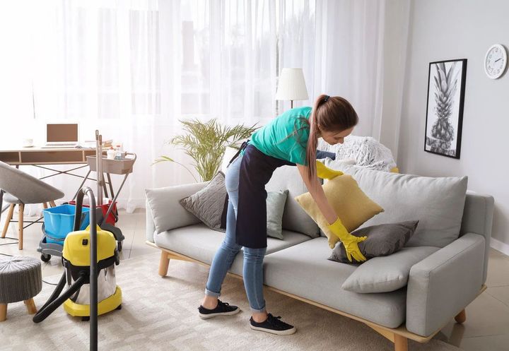 A woman is cleaning a couch in a living room.