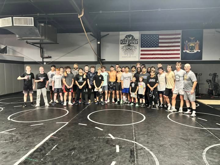 Group of people on a wrestling mat in a gym. An American flag and New York flag hang on the wall.
