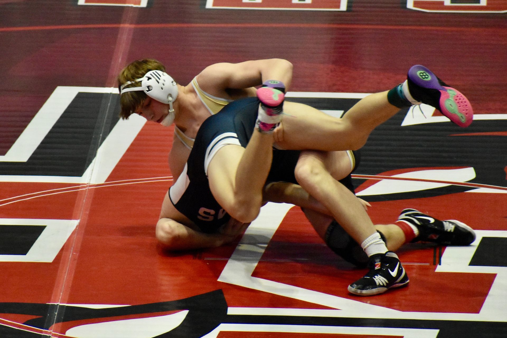 Group of people on a wrestling mat in a gym. An American flag and New York flag hang on the wall.