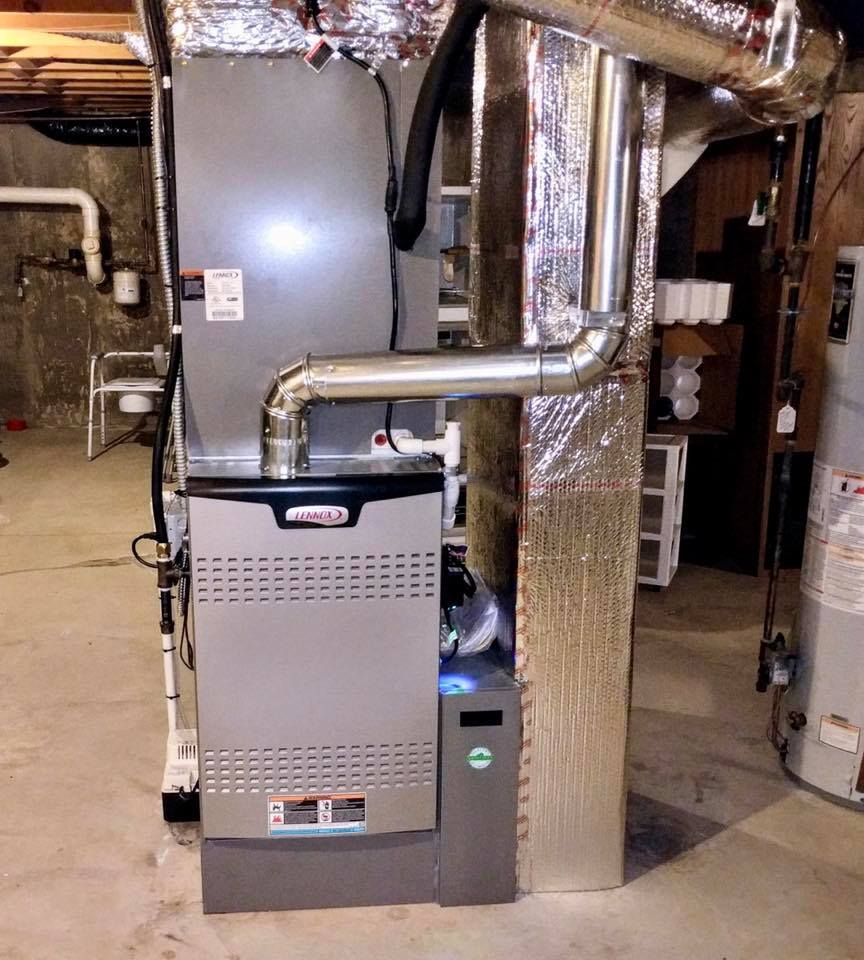 A gas furnace in a basement. It is silver and gray, with ductwork and a water heater nearby.
