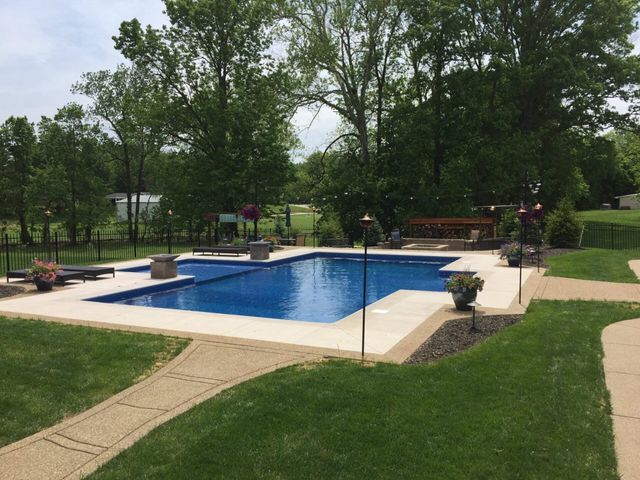 A large swimming pool in the middle of a lush green yard surrounded by trees.