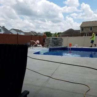 A man is standing next to a swimming pool in a backyard.