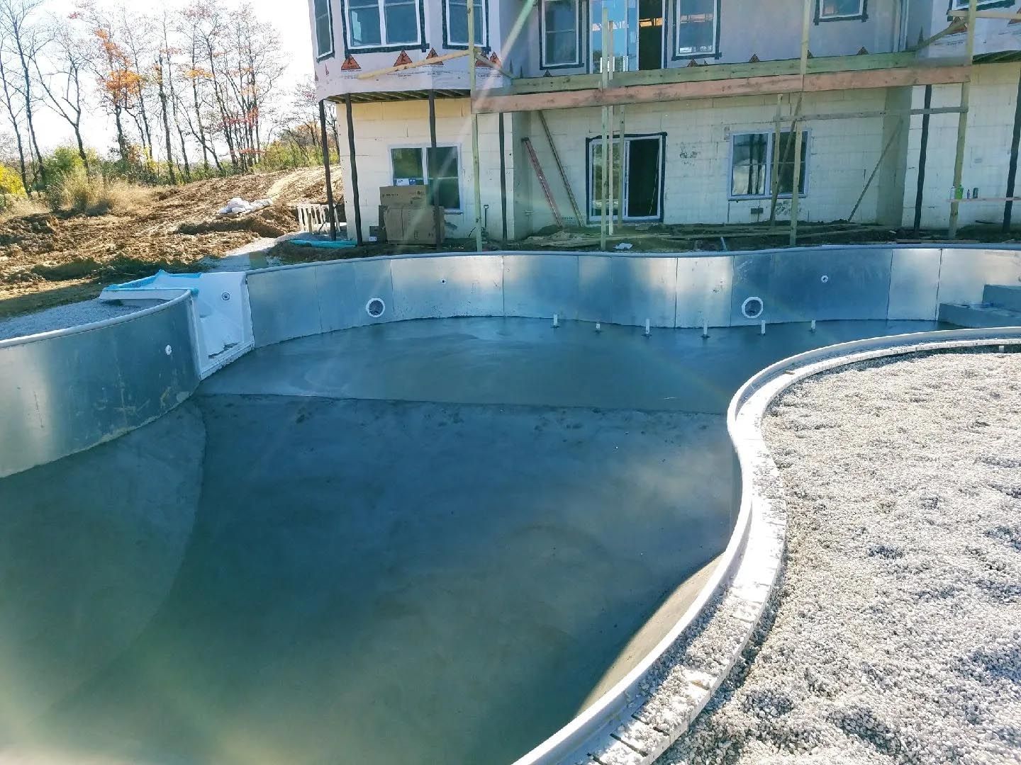 A large swimming pool is under construction in front of a house