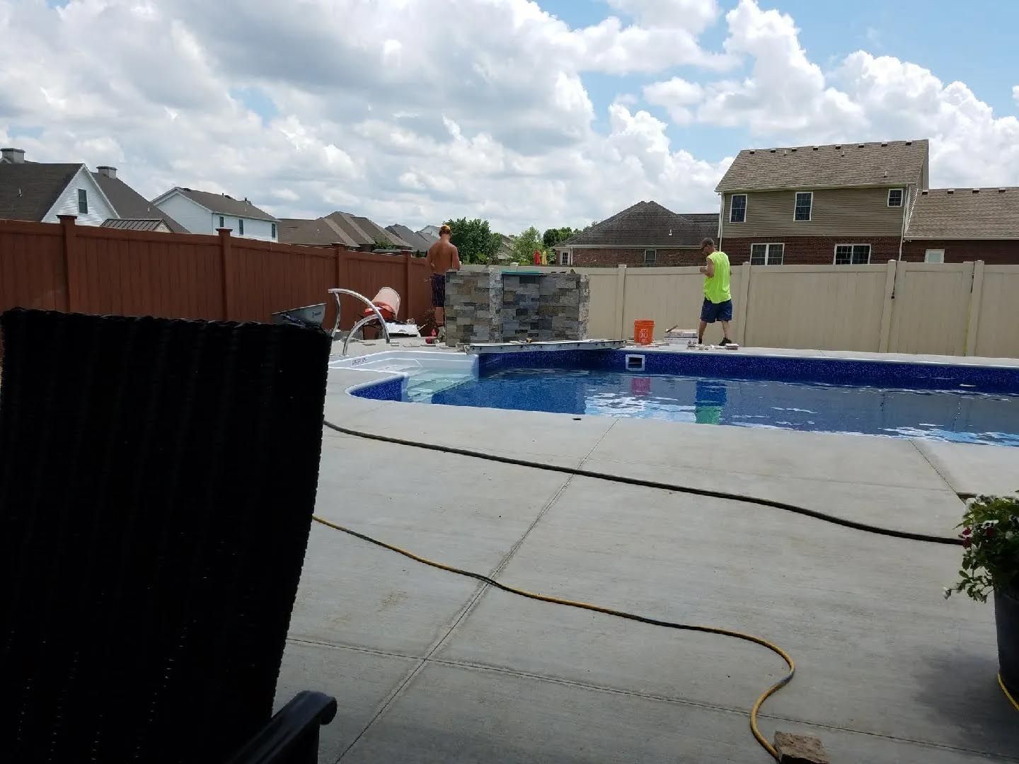 A man in a green shirt is standing next to a swimming pool