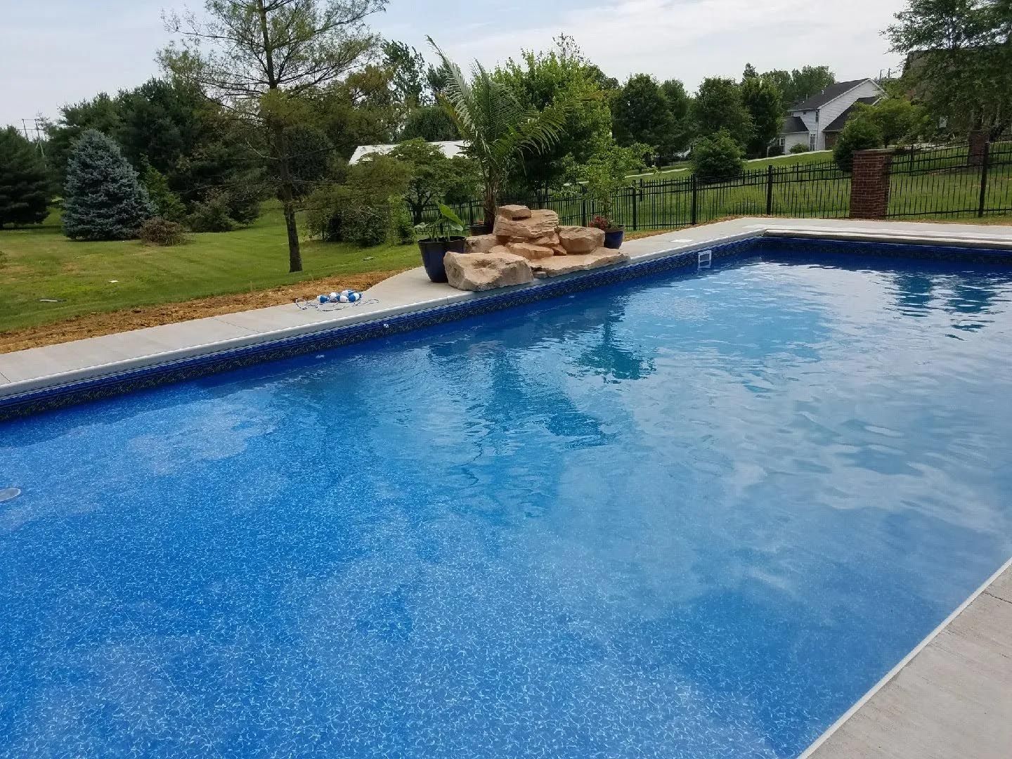 A large swimming pool is surrounded by trees and a fence.