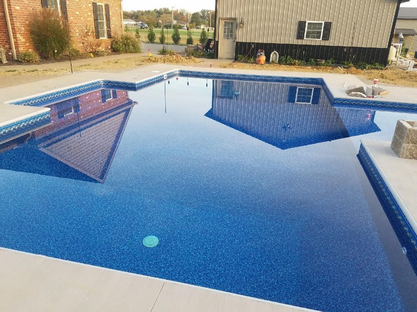 A large blue swimming pool with a house in the background