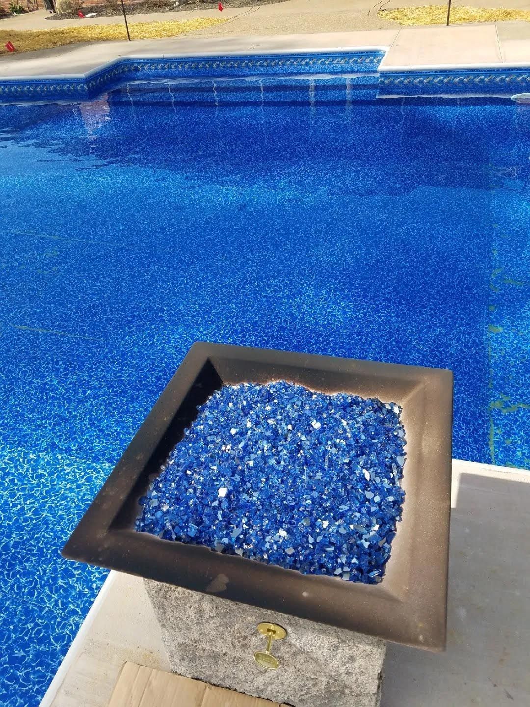 A planter filled with blue glass sits next to a swimming pool.