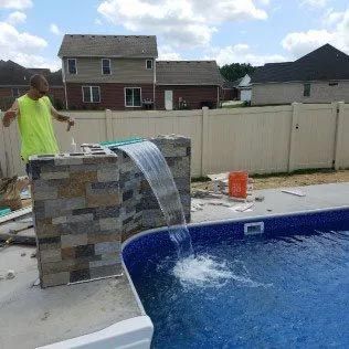 A man is working on a waterfall next to a swimming pool.