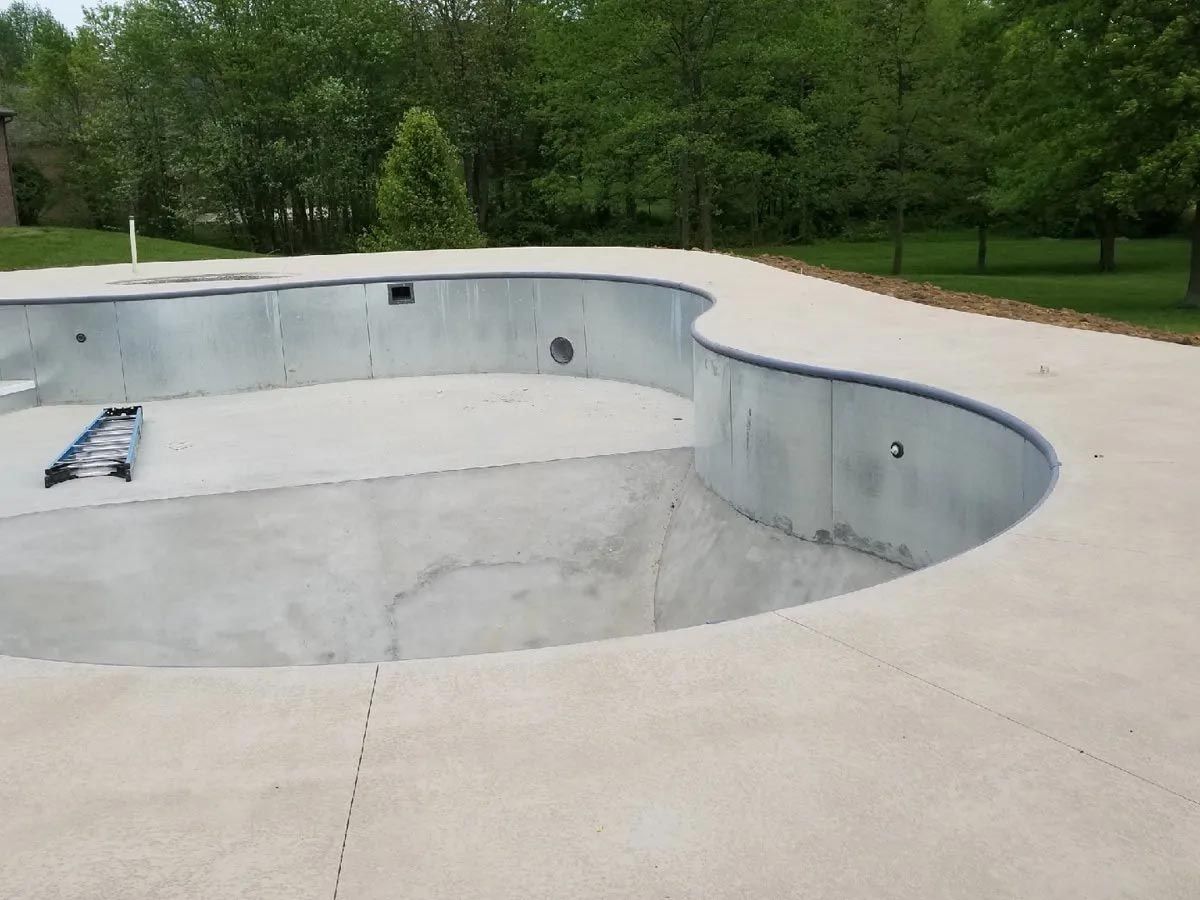 A swimming pool with a concrete deck and trees in the background.