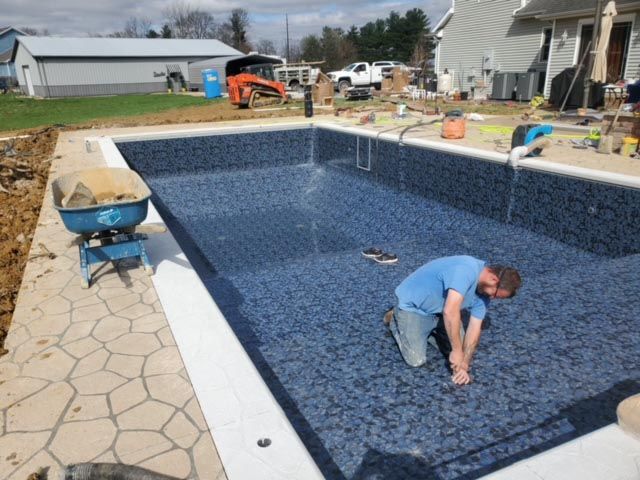 A man is kneeling in front of a swimming pool