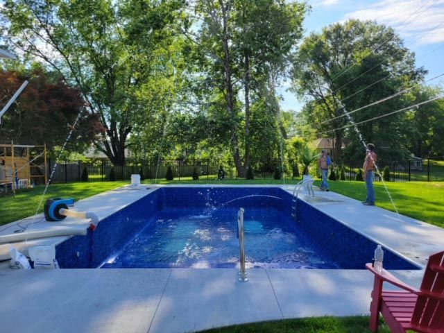 A man is standing next to a large swimming pool in a backyard.
