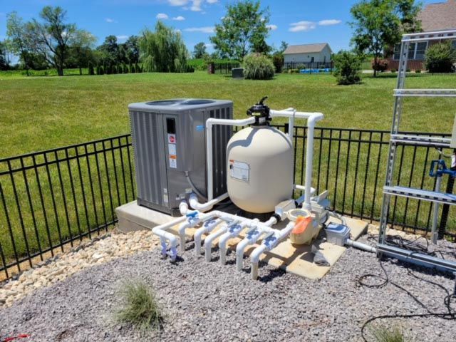 A pool filter is sitting next to an air conditioner in a backyard.