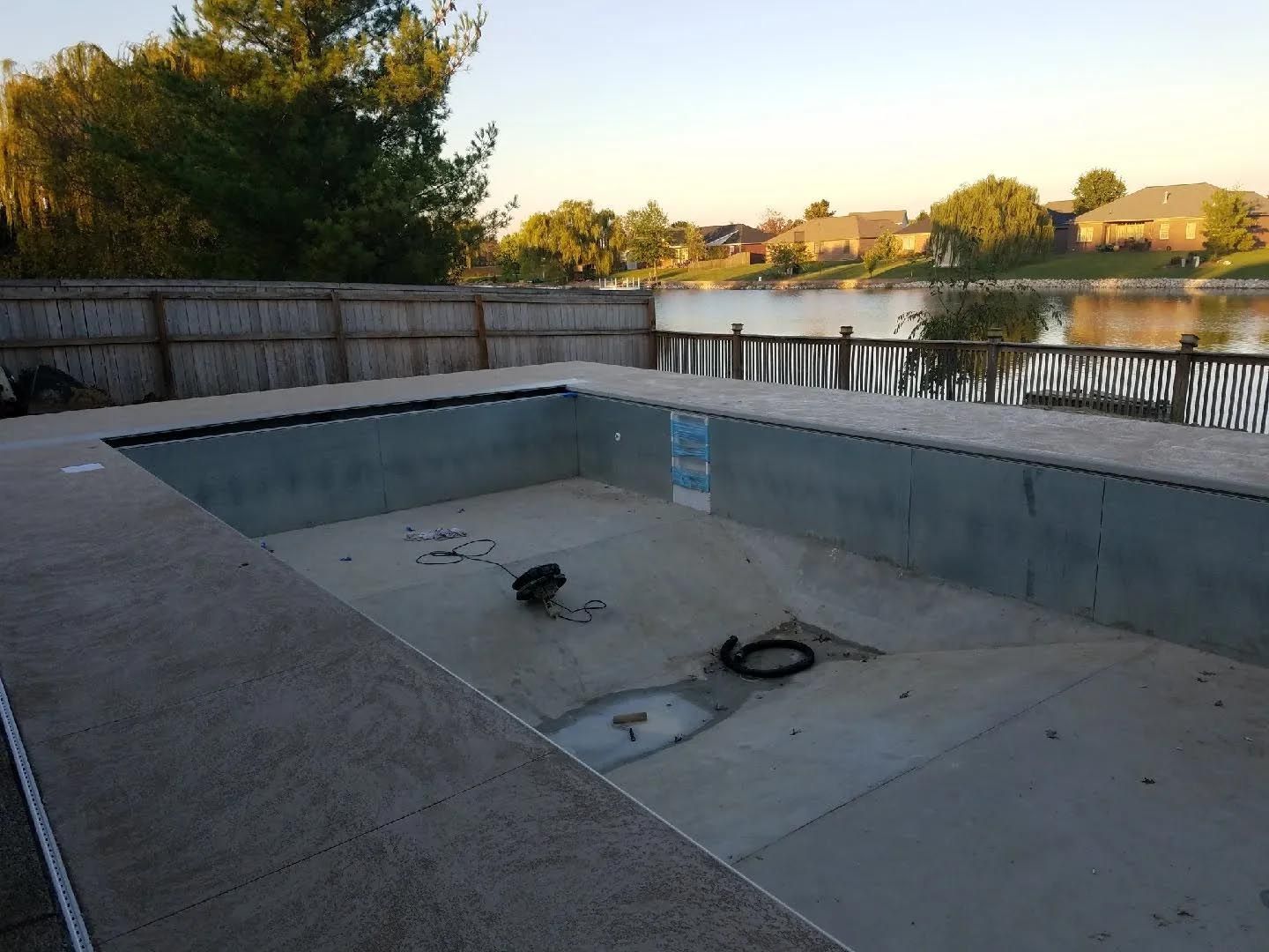 An empty swimming pool with a fence and a lake in the background.