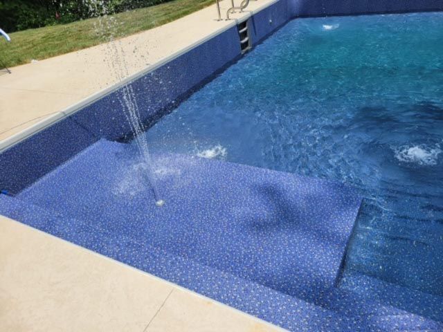 A swimming pool with stairs and a fountain in the middle