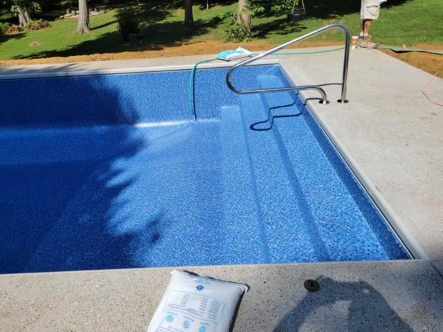 A blue swimming pool with stairs and a hose attached to it