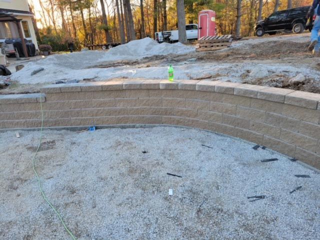 A brick wall is being built in the dirt in front of a house.