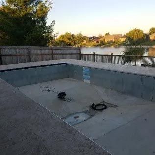 An empty swimming pool with a fence and a lake in the background.
