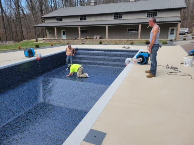 Two men are working on a swimming pool in front of a house