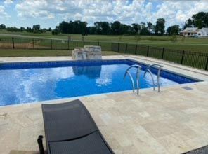 A large swimming pool is surrounded by a fence and a chair.