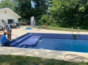 Two men are working on a swimming pool in a backyard.