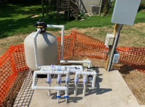 A swimming pool filter is sitting on top of a concrete platform next to a fence.