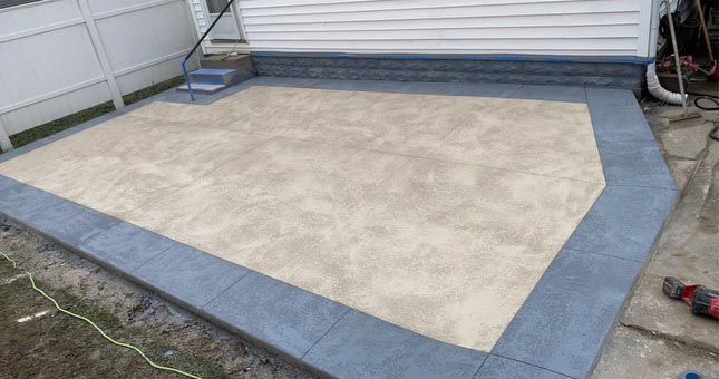 A patio with a blue border is being built in front of a house.