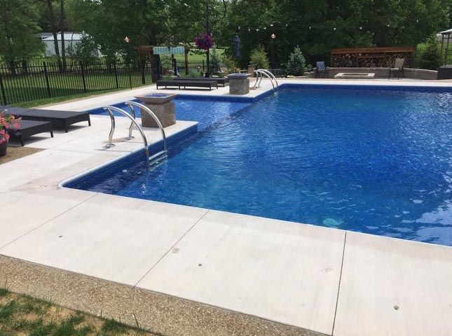 A large swimming pool with a concrete patio and chairs around it.