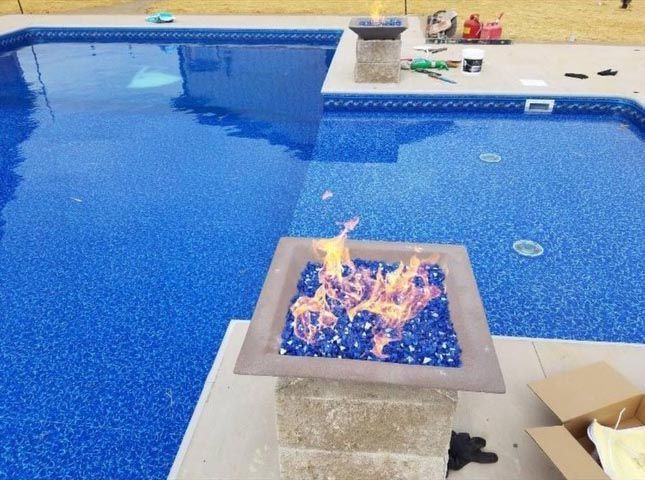 A fire pit in front of a large swimming pool